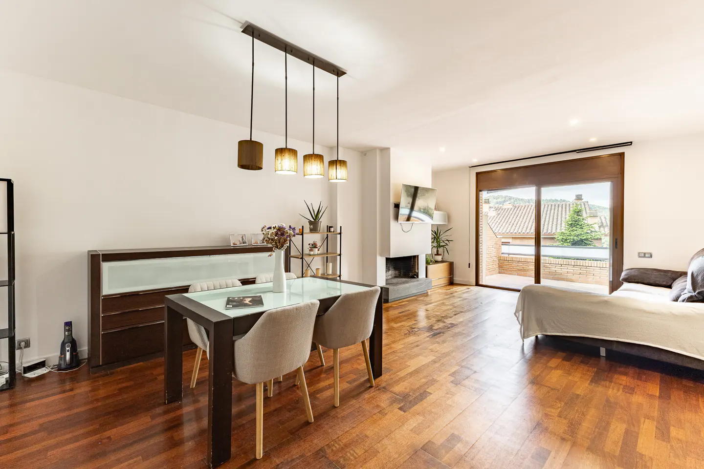 Bright living room with hardwood floors, a dining table with four chairs, and a sofa near a sliding glass door to a balcony.