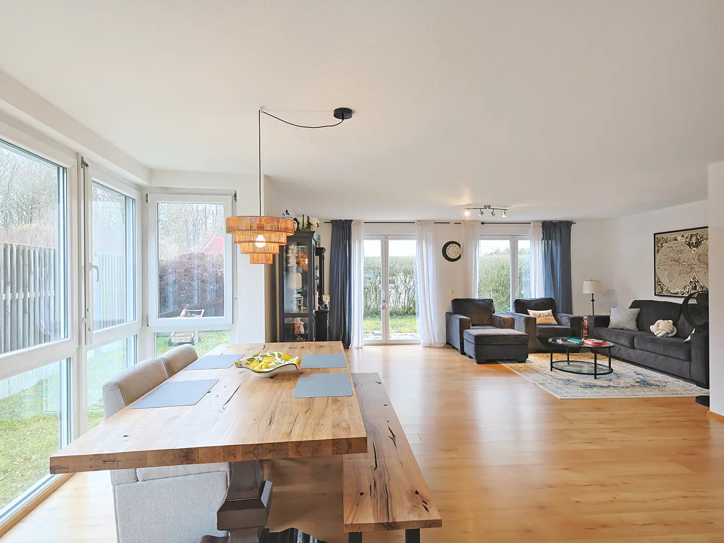 Open-concept living space with wood floors, a dining table with bench seating, and a gray sofa in the background.