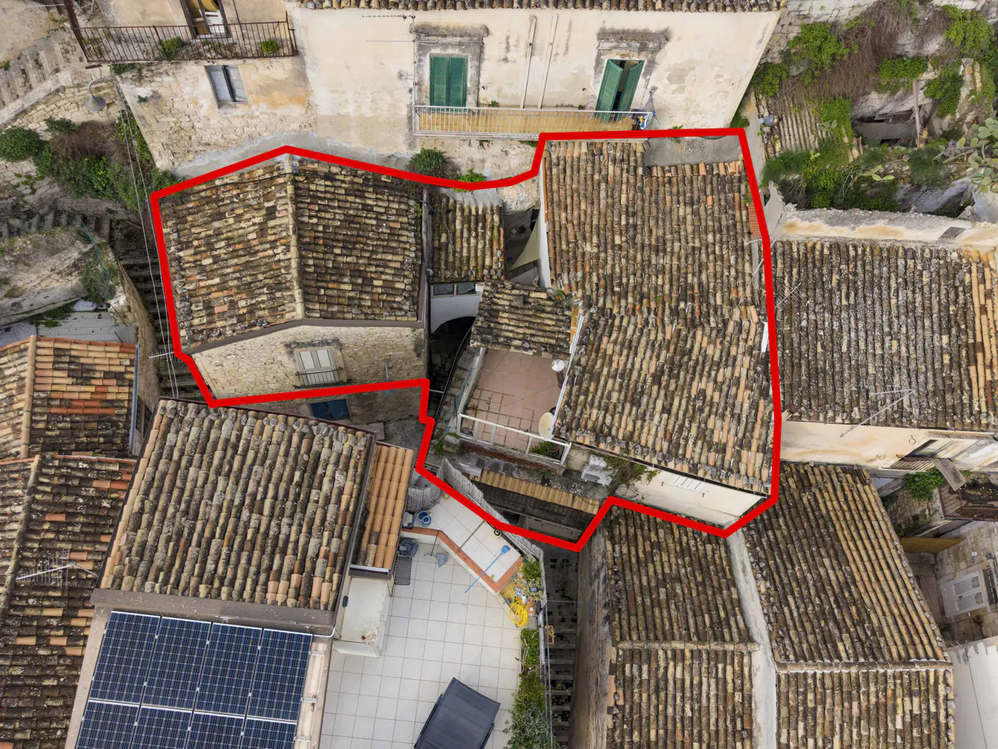 Aerial view of a stone building with terracotta tile roofs, outlined in red, nestled among historic Mediterranean homes.