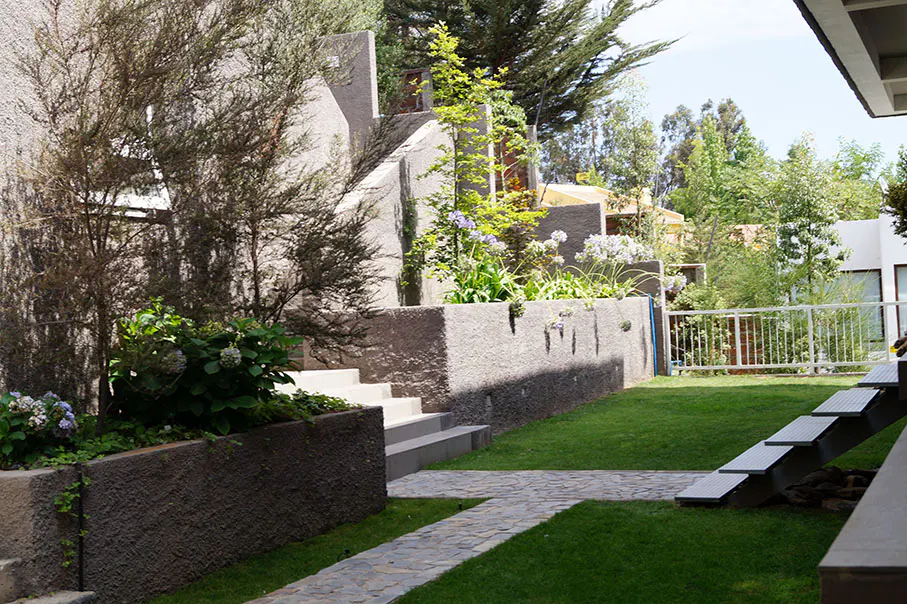 A backyard with a stone path, green grass, and tiered concrete planters with flowers and trees.