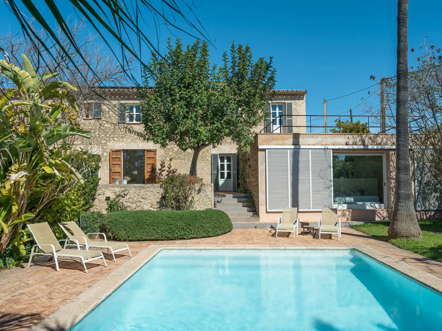 Exterior view of a stone house with a blue swimming pool and lounge chairs in the foreground.