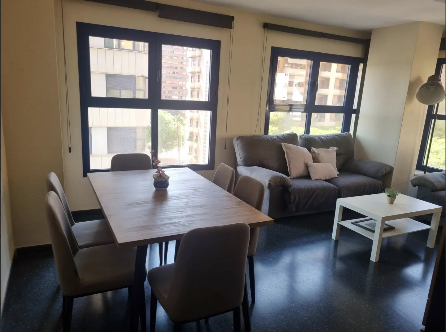 Dining area with a wooden table and six chairs next to a living room featuring a grey sofa and white coffee table.