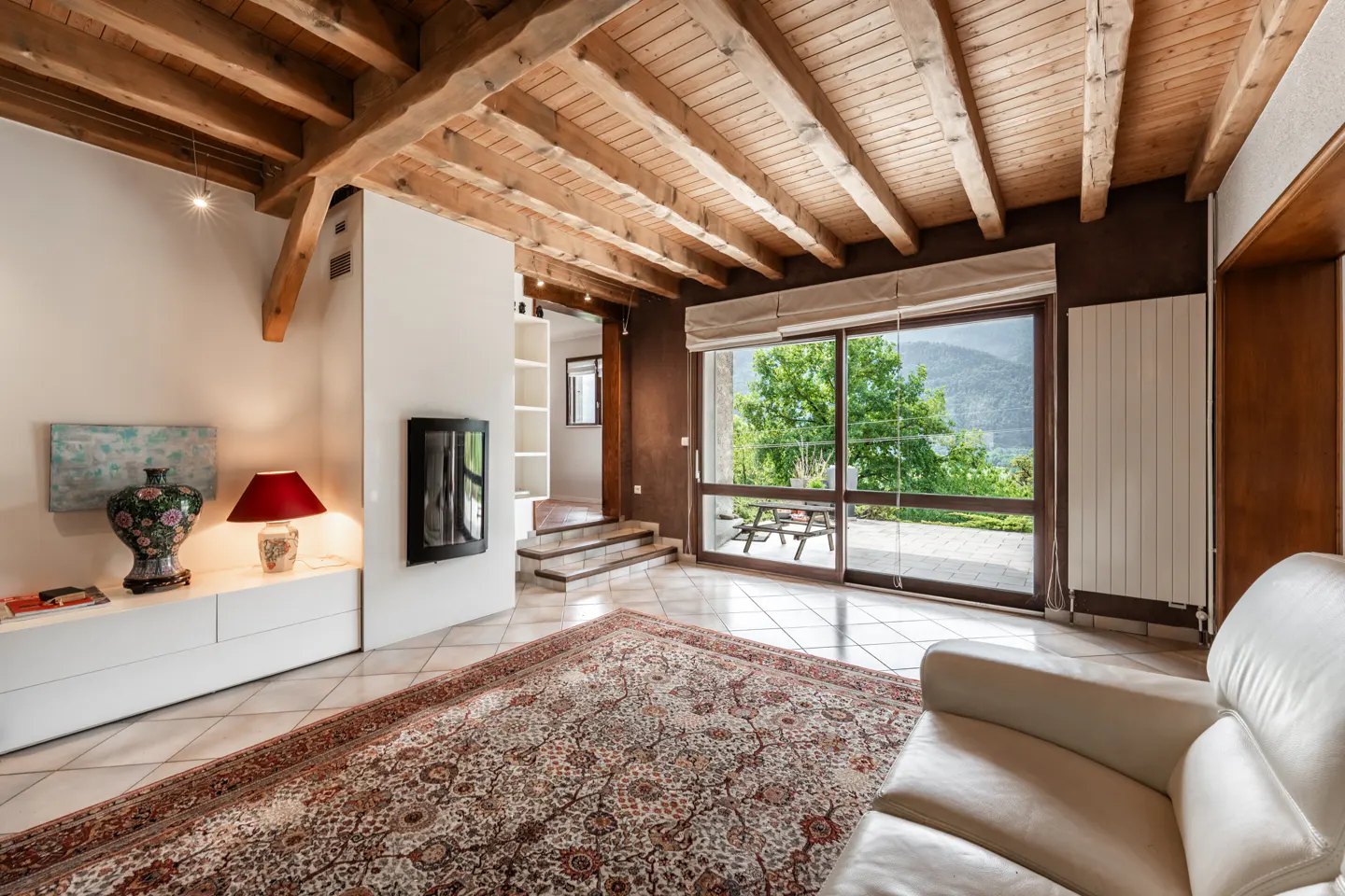 Living room with exposed wood beams, white tile floor, and large sliding glass doors to a patio with mountain views.