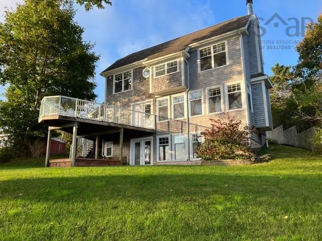 Exterior view of a two-story house with gray shingles, a deck, and a green lawn on a sunny day.