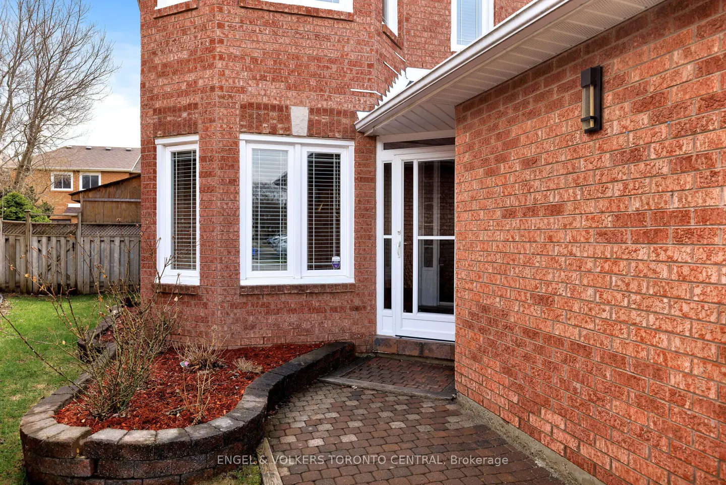 Exterior view of a red brick house with white trim, windows, and a front door. A brick walkway leads to the entrance.