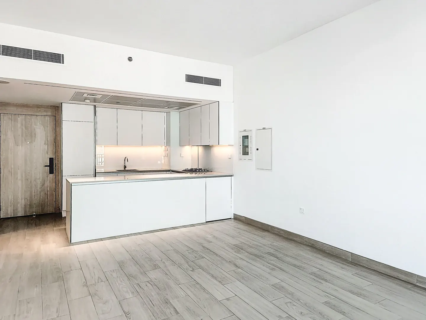 A bright, modern kitchen with white cabinets, light wood floors, and a door on the left.