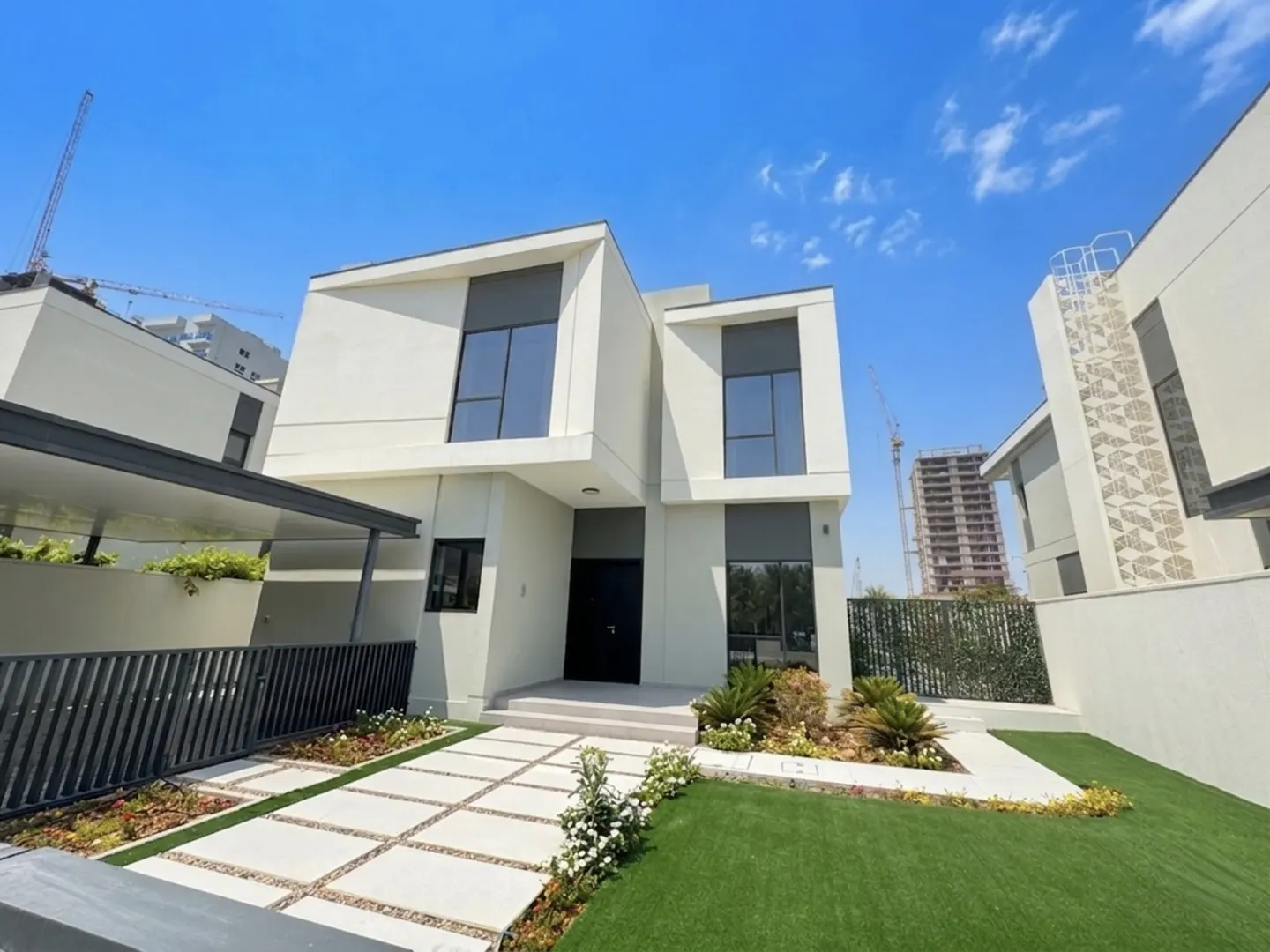 Modern two-story white house with a black front door and large windows. A walkway of square pavers leads to the entrance, surrounded by green grass.