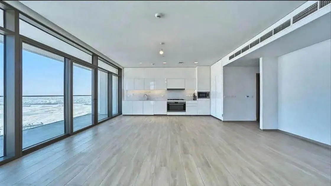 Bright, empty apartment with white kitchen, wood floors, and floor-to-ceiling windows overlooking a snowy landscape.