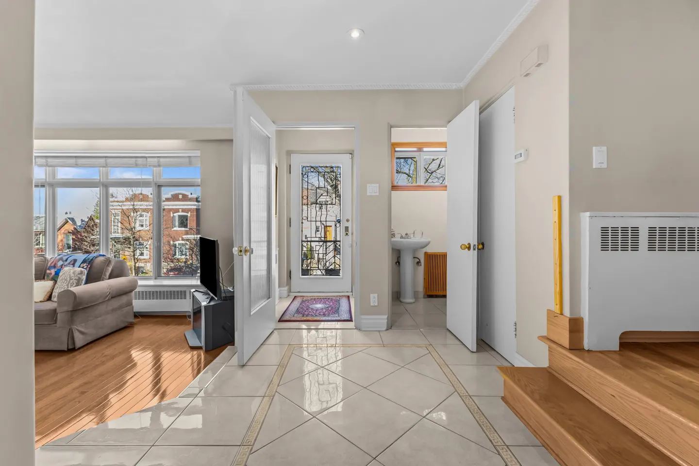 Foyer with tile floor, open white doors to living room and powder room. Front door with decorative glass. Stairs to the right.