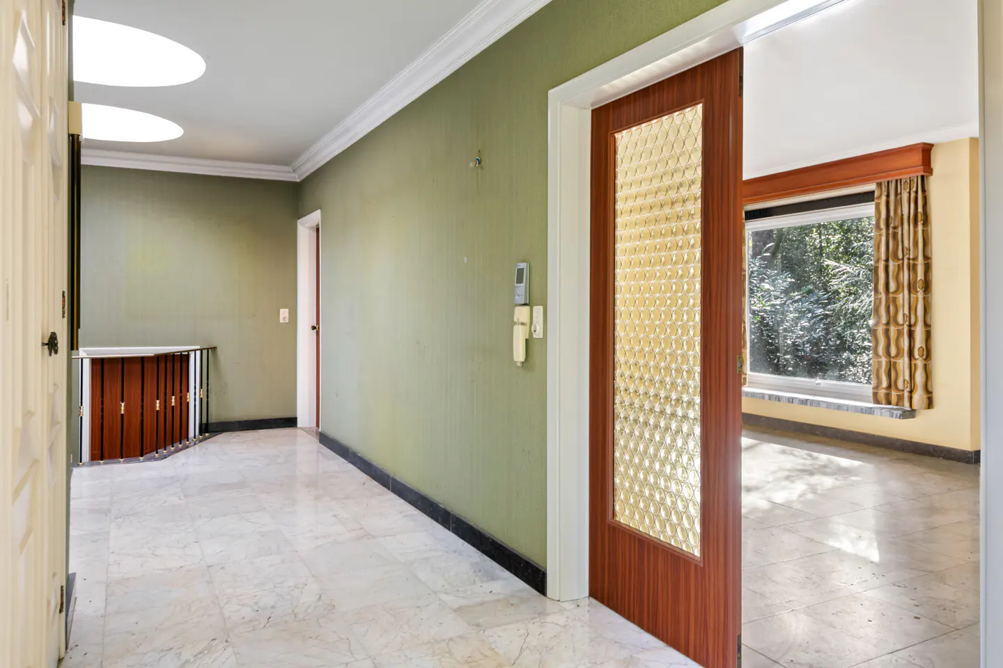 Hallway with marble floors, olive green walls, and a wood-framed glass door leading to a room with a window.