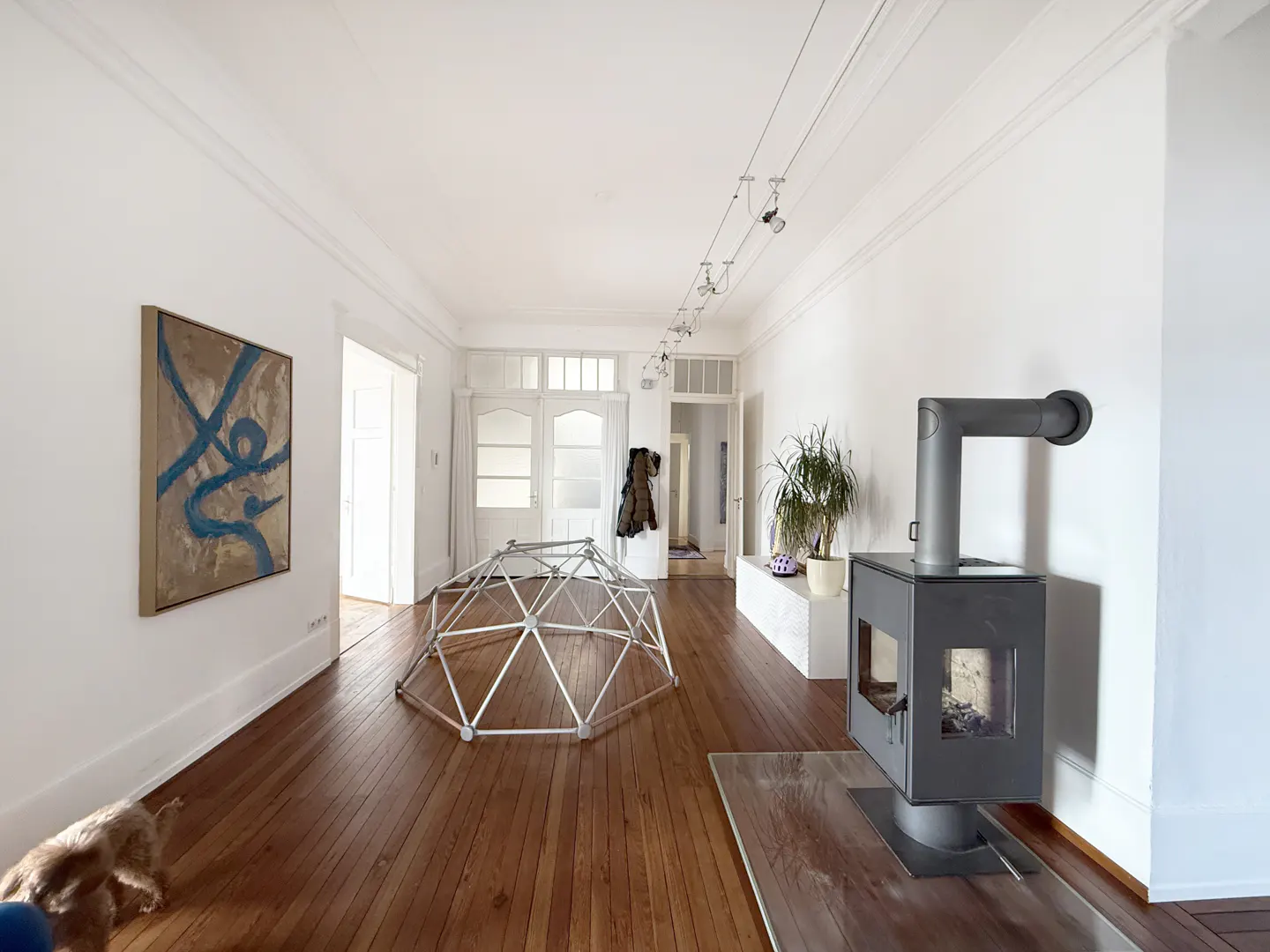 Bright, airy room with wood floors, white walls, and a modern wood-burning stove. A geodesic dome sits in the center, with art and plants adding character.