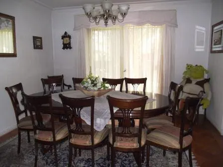 A dining room with a dark wood table and chairs, a chandelier, and a Shrek doll in the corner.