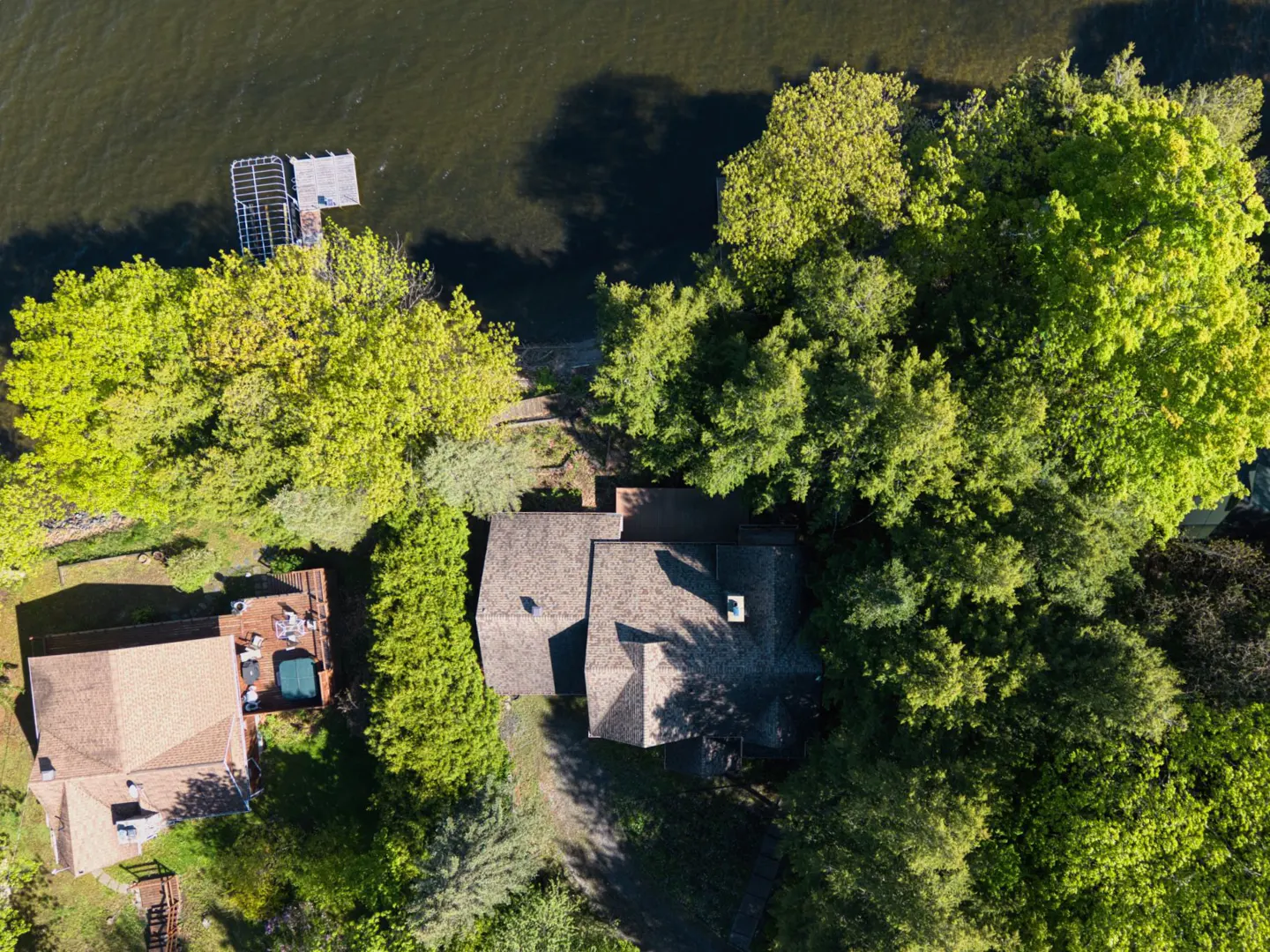 Aerial view of a brown-roofed house surrounded by green trees, next to a lake with a dock.