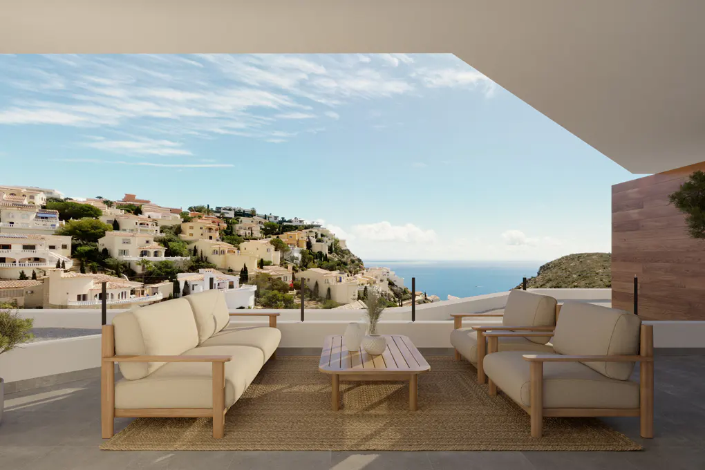 Balcony view with beige sofa, chairs, and table on a jute rug. Ocean and hillside homes in the background under a blue sky.