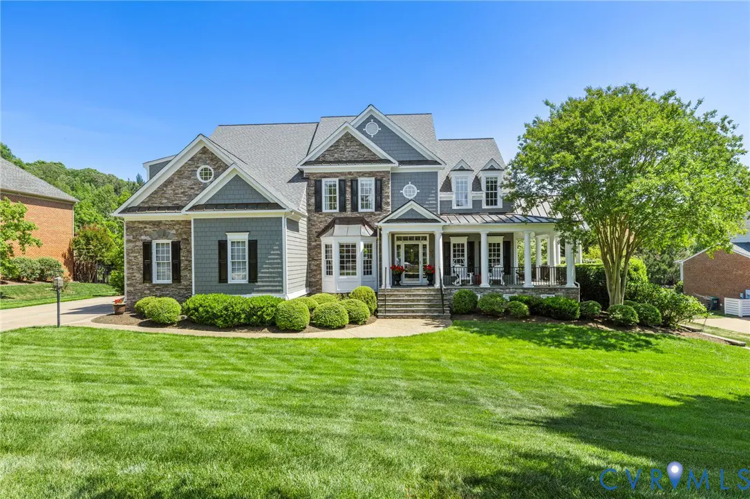 Two-story house with gray roof, stone and gray siding, black shutters, and a white porch with columns. Green lawn in front.