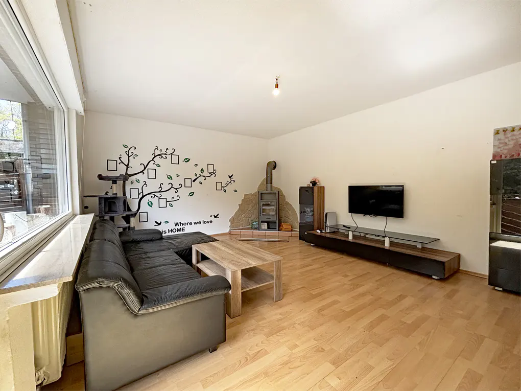 A living room with a black sofa, wood floors, a TV, and a wood-burning stove. A tree decal is on the wall.
