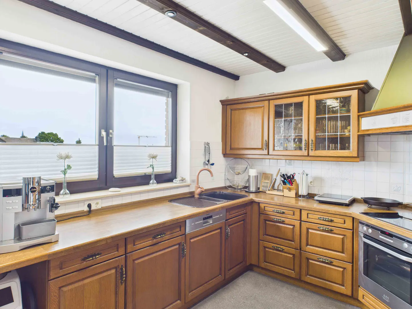 A bright kitchen with wooden cabinets, a copper faucet, and a large window.