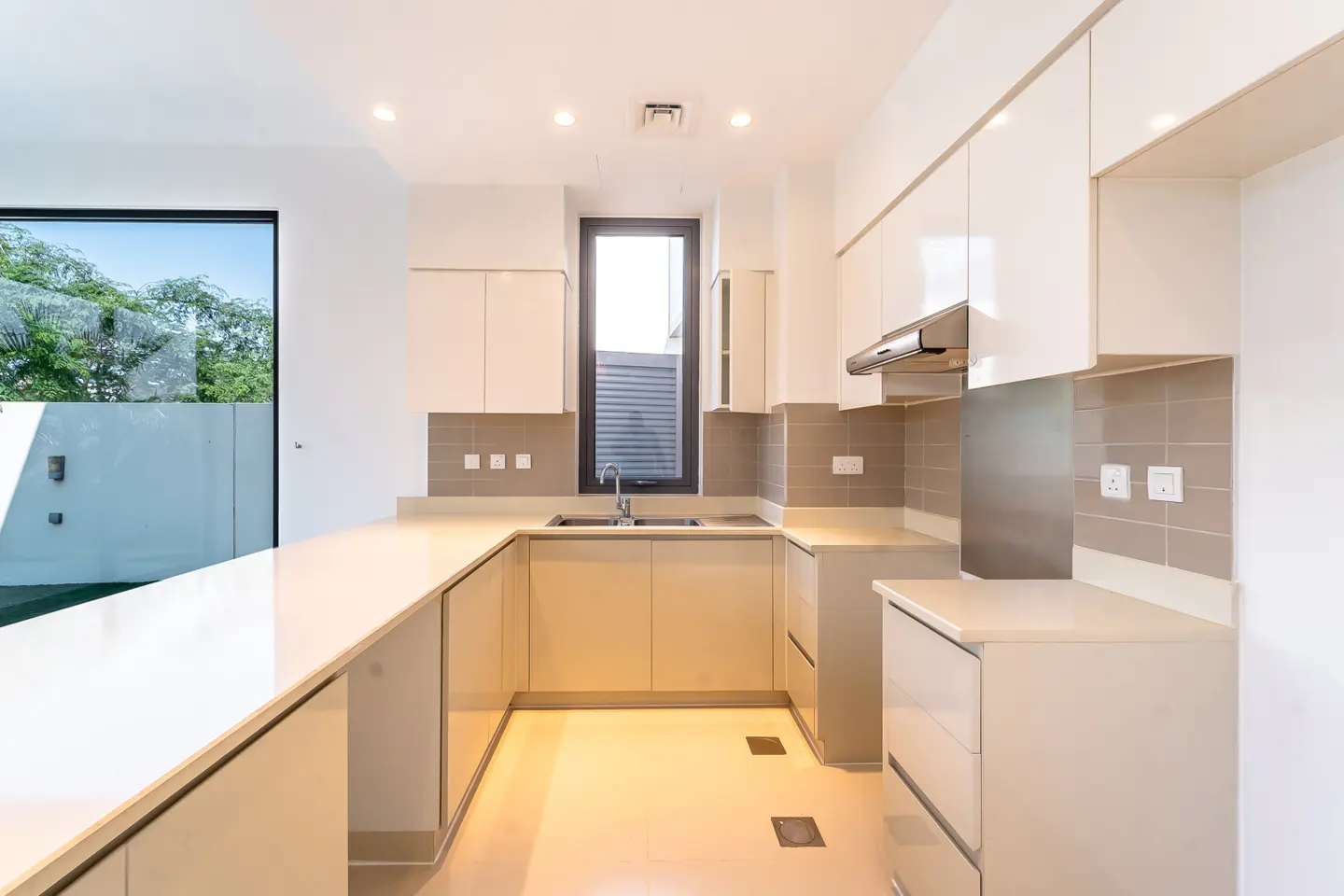 Bright, modern kitchen with white cabinets, light countertops, and stainless steel appliances. A large window offers a view of greenery.