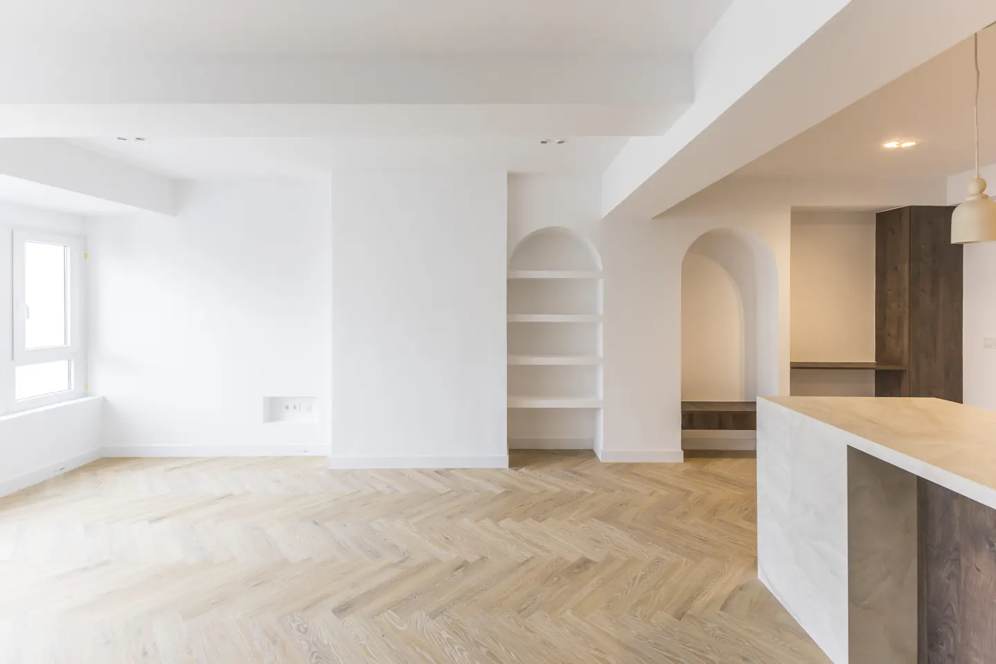 Bright, modern interior with white walls, herringbone wood floors, arched shelving, and a kitchen island with a light countertop.