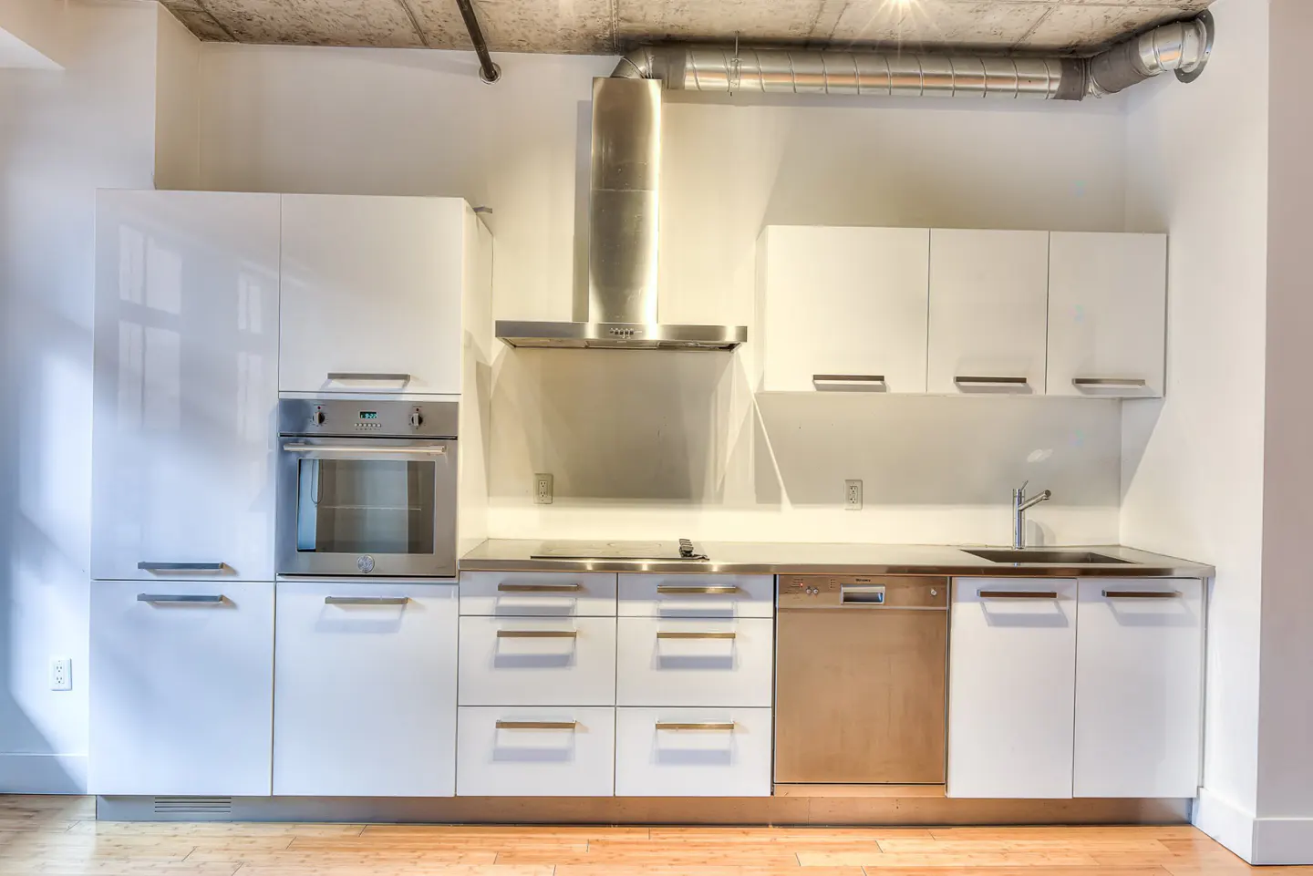 A modern kitchen with white cabinets, stainless steel appliances, and a concrete ceiling.