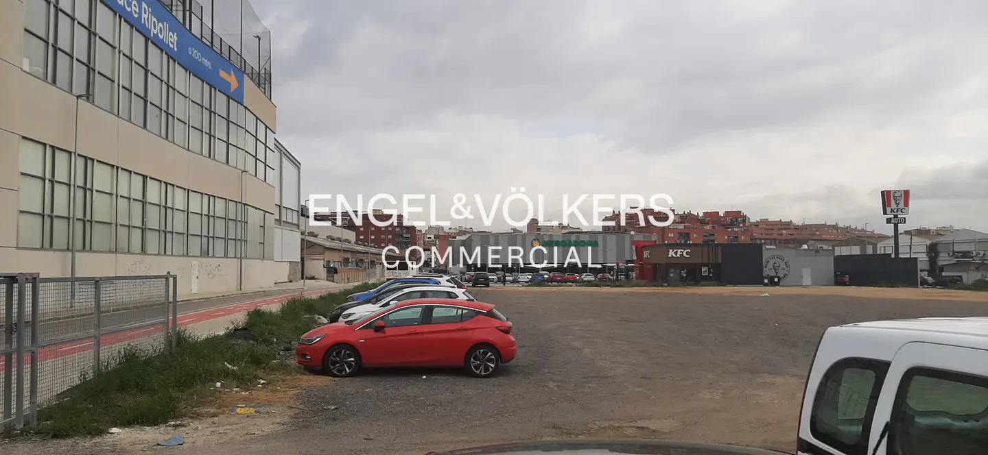 Commercial property with a parking lot, cars, and a KFC restaurant in the background. The sky is cloudy.
