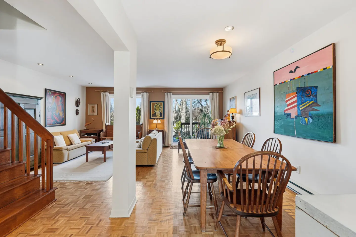 Open-concept living and dining area with wood floors, stairs, and a large colorful painting. A wooden table is set for six.