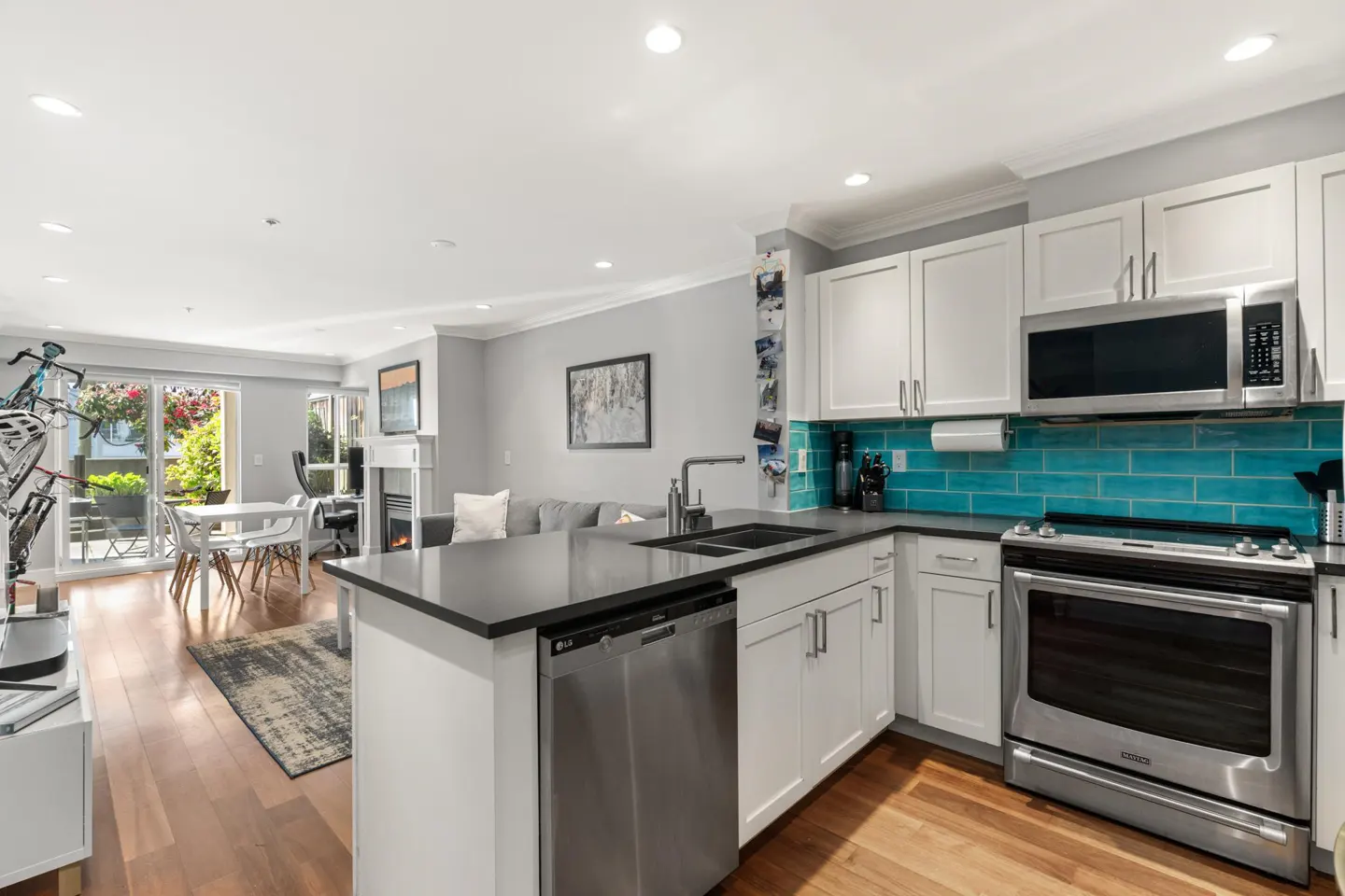 Open concept living space with a kitchen featuring white cabinets, turquoise backsplash, and stainless steel appliances.