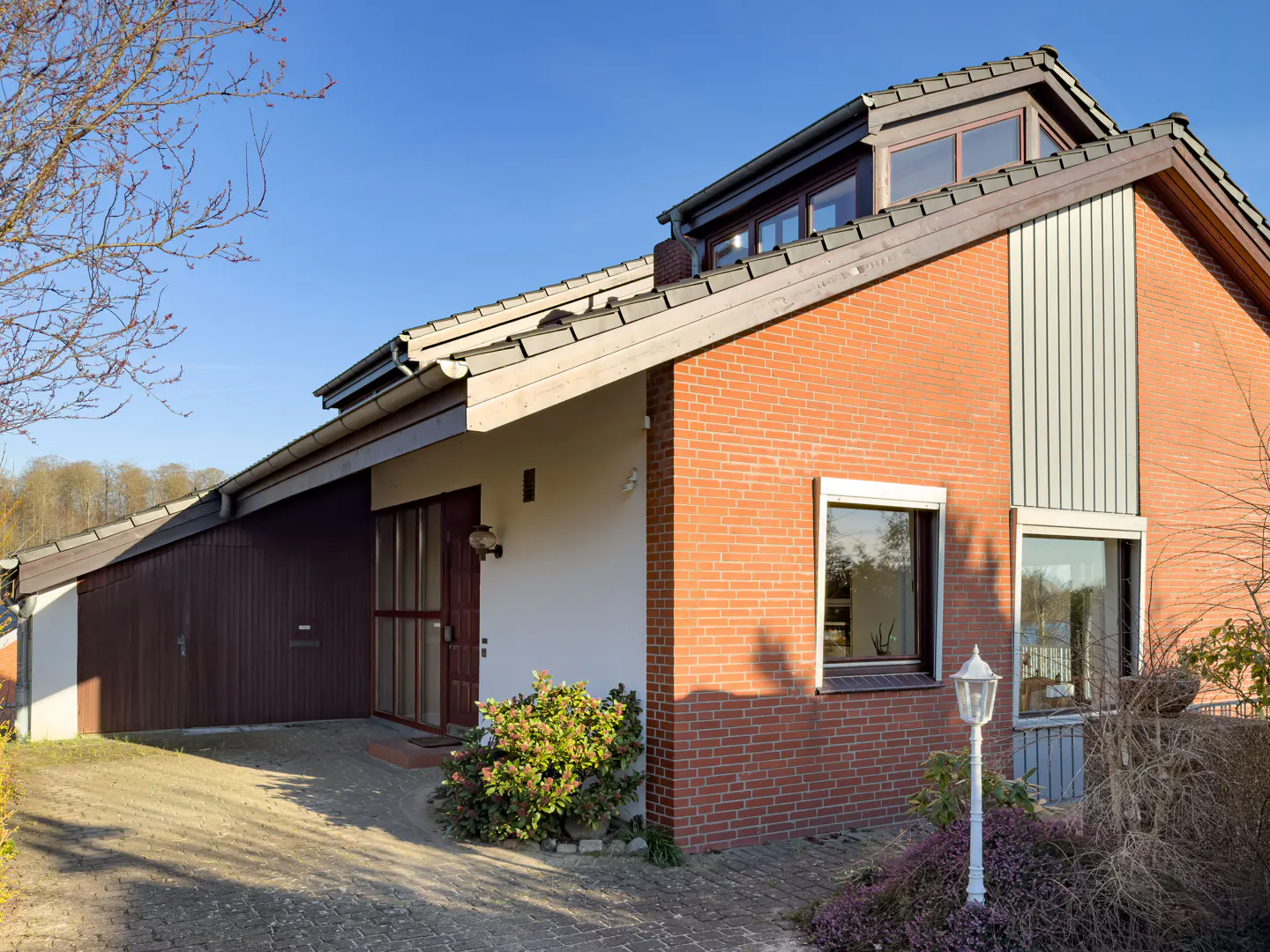 Exterior view of a one-story house with a brick facade, white trim, and a brown garage door under a blue sky.