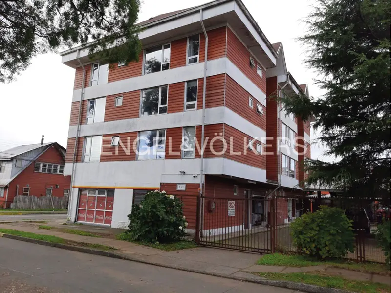 Exterior view of a four-story apartment building with red wood paneling and white trim, featuring an Engel & Völkers logo.