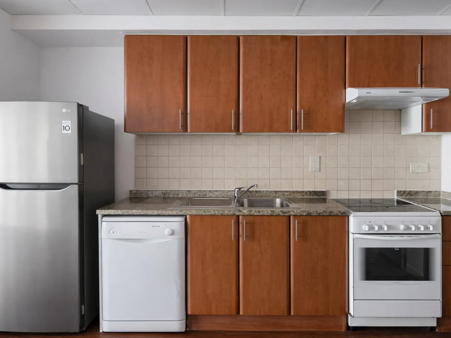 Kitchen with wood cabinets, stainless steel fridge, white dishwasher, white stove, and tiled backsplash.