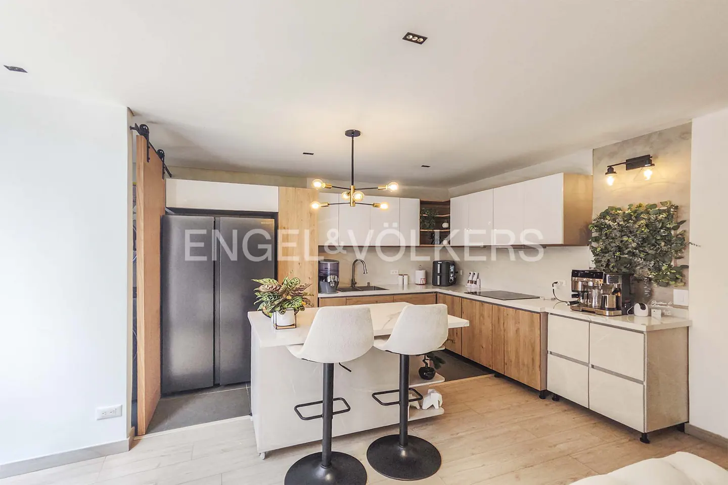 A modern kitchen with white cabinets, wood accents, a marble island with two stools, and stainless steel appliances.