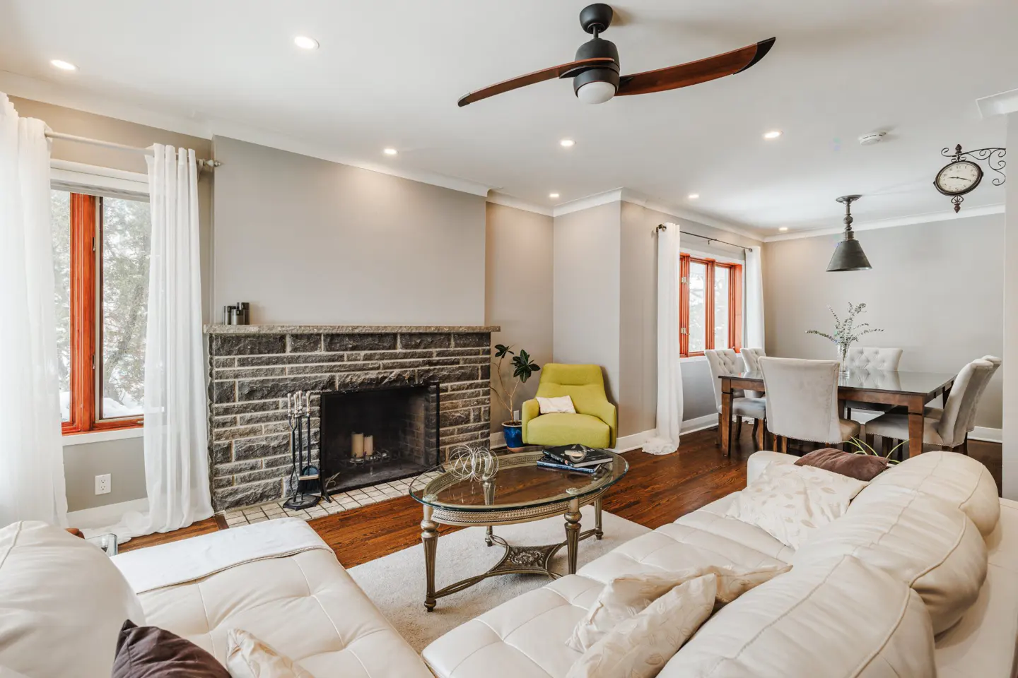 Living room with stone fireplace, white sofa, and hardwood floors. A dining area is visible in the background.