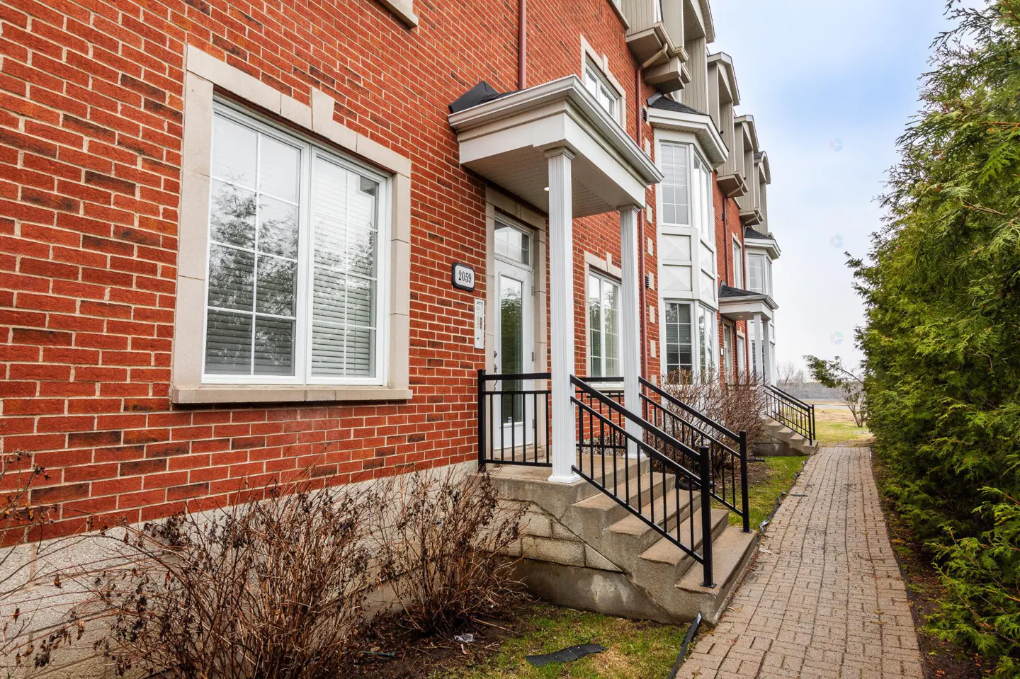 Exterior view of red brick townhouses with white trim, black railings, and a brick walkway.