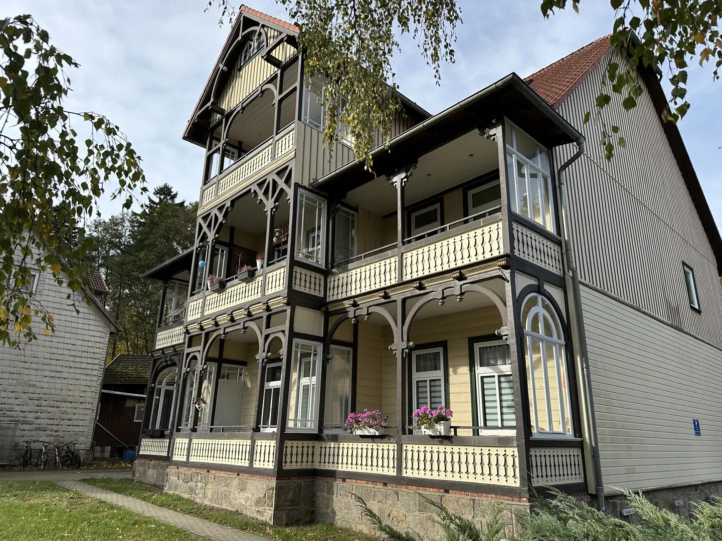A three-story house with a brown roof, yellow siding, and dark brown trim. It has balconies on each floor with decorative railings and arched supports.