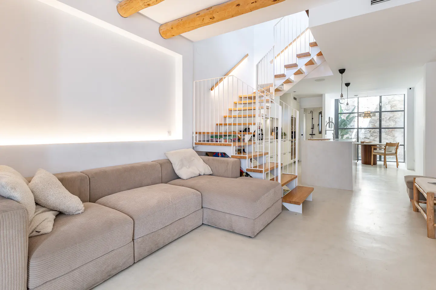 Bright, modern living room with a beige sectional sofa, white walls, and a wooden spiral staircase with white railings.