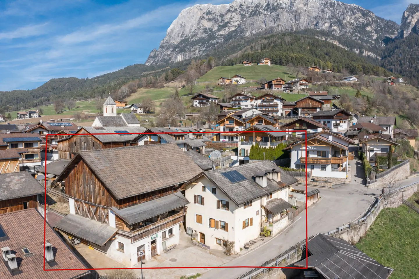 Aerial view of a property outlined in red, nestled in a village with mountains in the background.