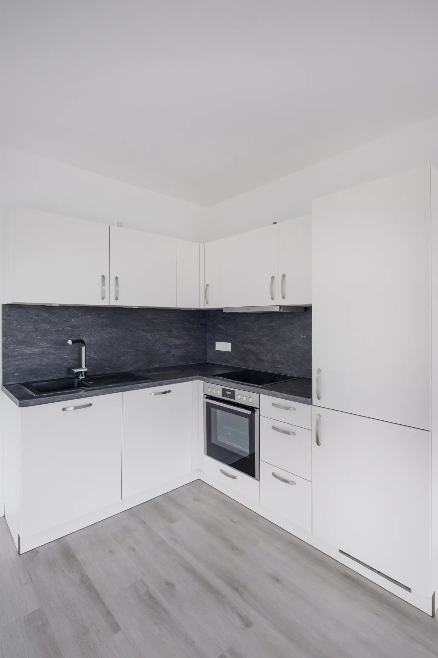 Bright kitchen with white cabinets, gray countertops and wood-look flooring. Sink, oven, and drawers are visible.