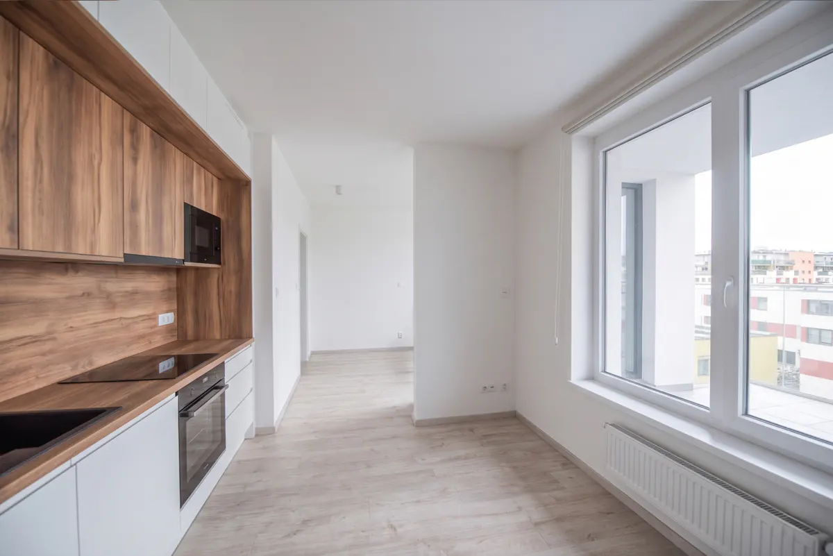 Modern kitchen with white cabinets, wood-grain backsplash, built-in oven, and a large window overlooking city buildings.