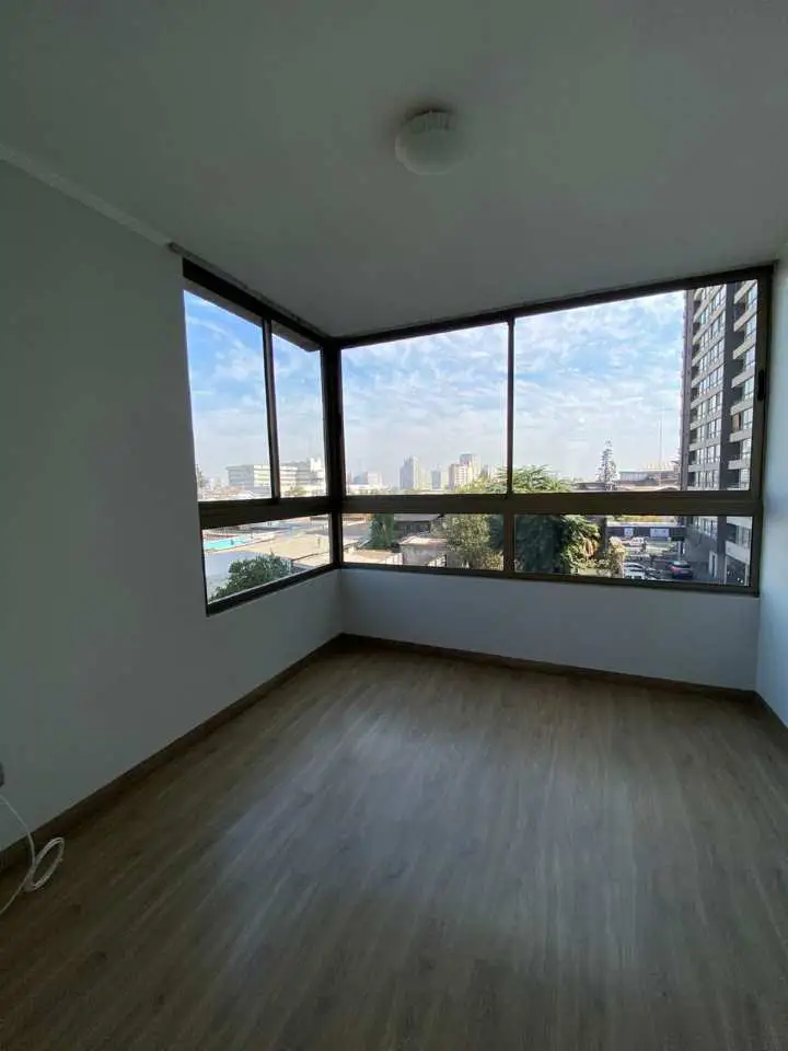 Empty room with light wood floors and white walls. Large windows offer a city view.