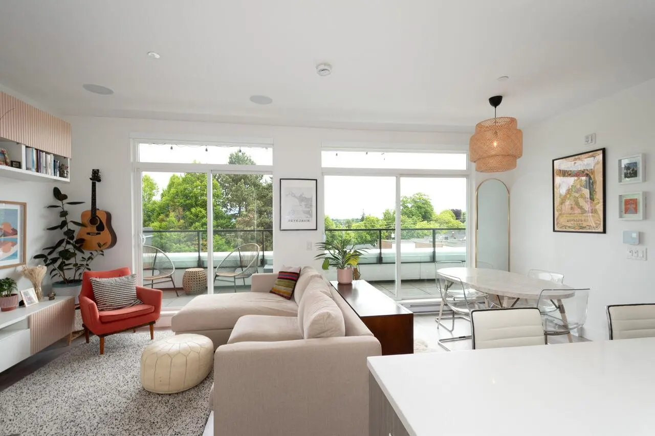 Bright living room with a beige sectional, coral armchair, dining area, and sliding glass doors leading to a balcony.