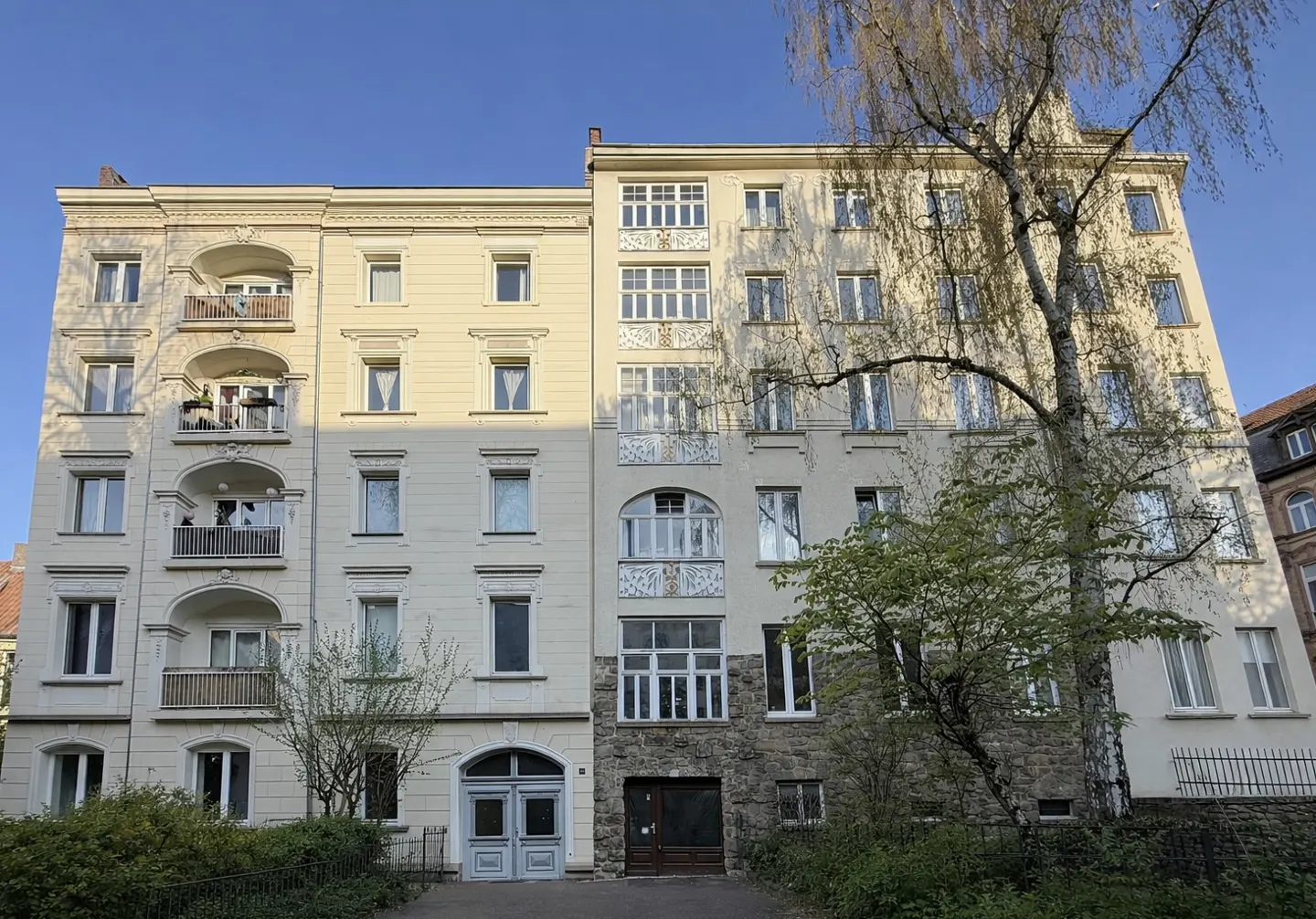 Exterior shot of a cream-colored apartment building with balconies, windows, and a blue sky background.