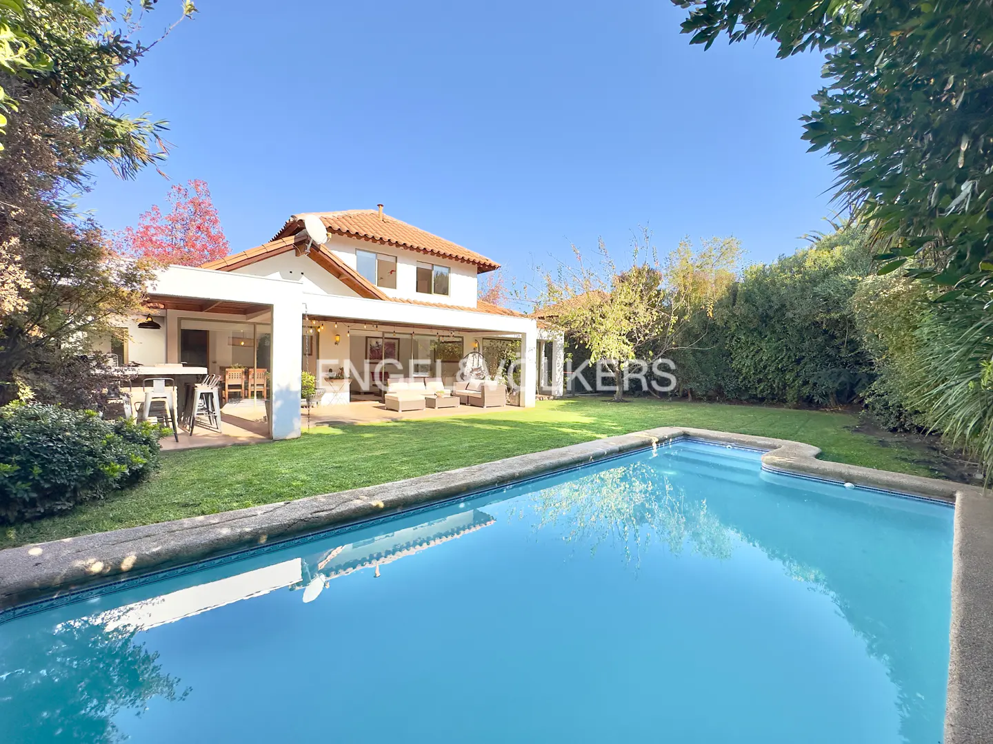 Backyard view of a two-story white house with a red tile roof, a pool, and green grass.
