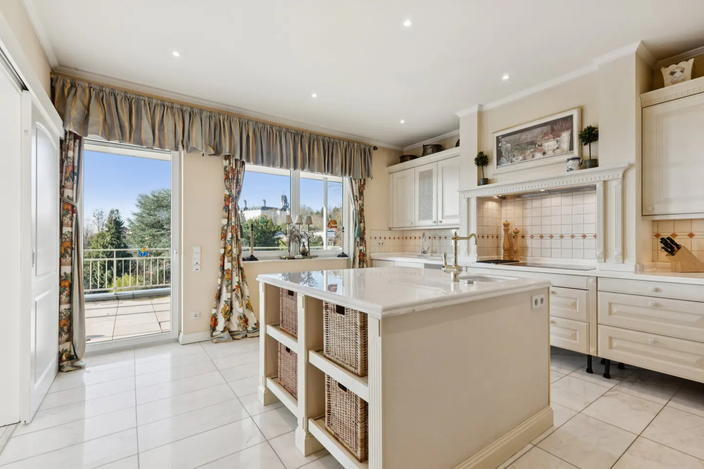 A bright, spacious kitchen with white cabinets, a marble island with wicker baskets, and a balcony view.