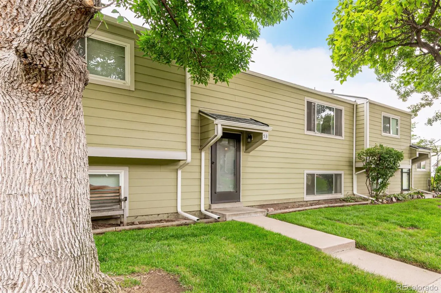 Exterior view of a light green two-story townhouse with a black front door, a concrete walkway, and green grass.