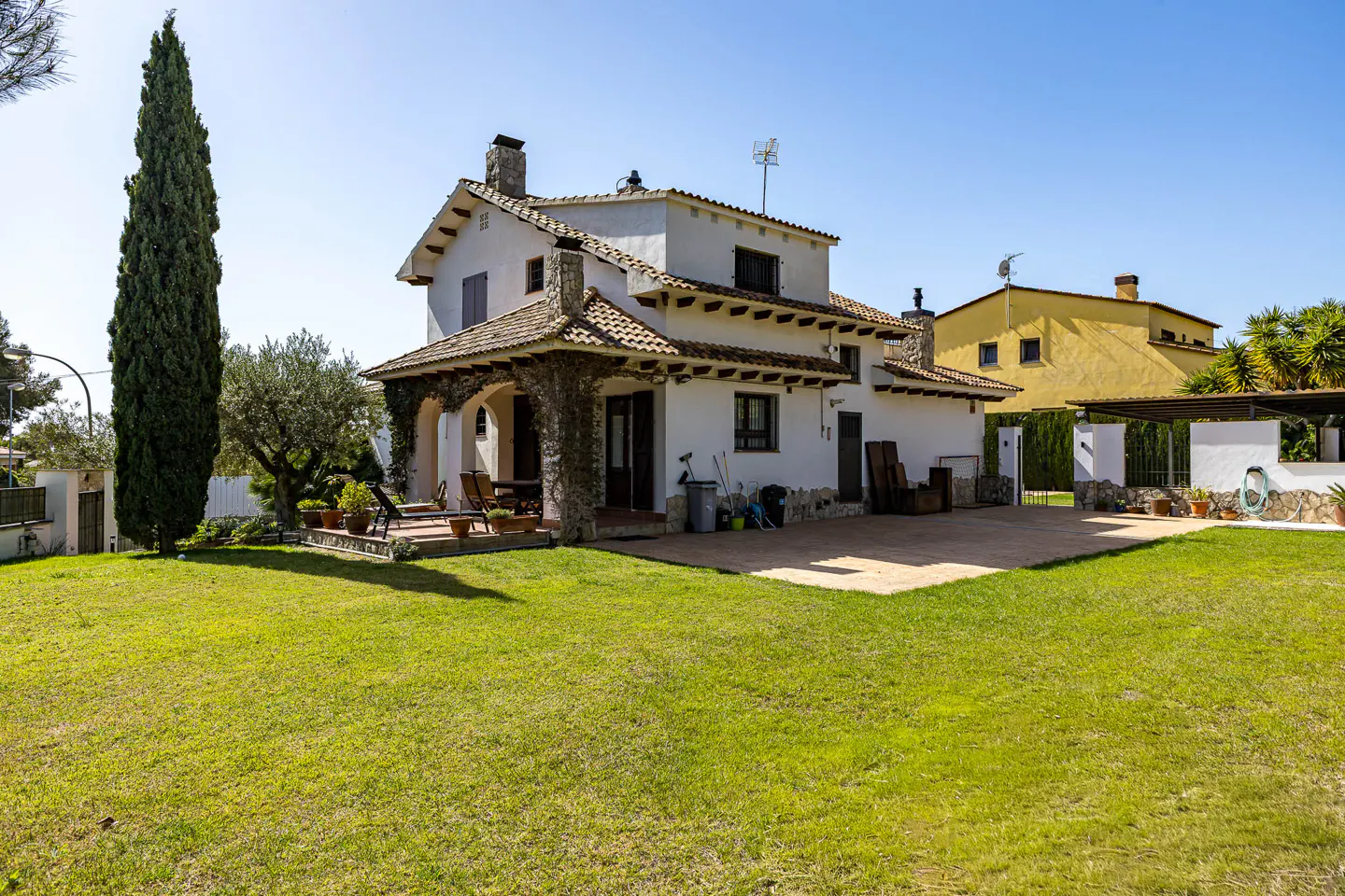 Two-story white house with a brown tile roof, stone accents, and a green lawn under a blue sky.