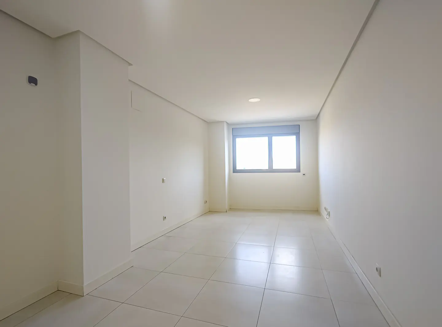 Bright, empty room with white walls, tile floor, and a window with gray frame.