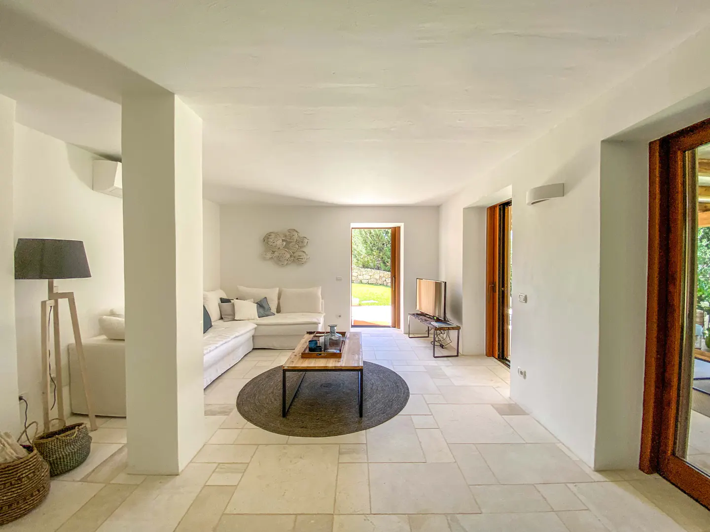 Bright, minimalist living room with white walls, stone floors, a white sectional sofa, and a wooden coffee table.