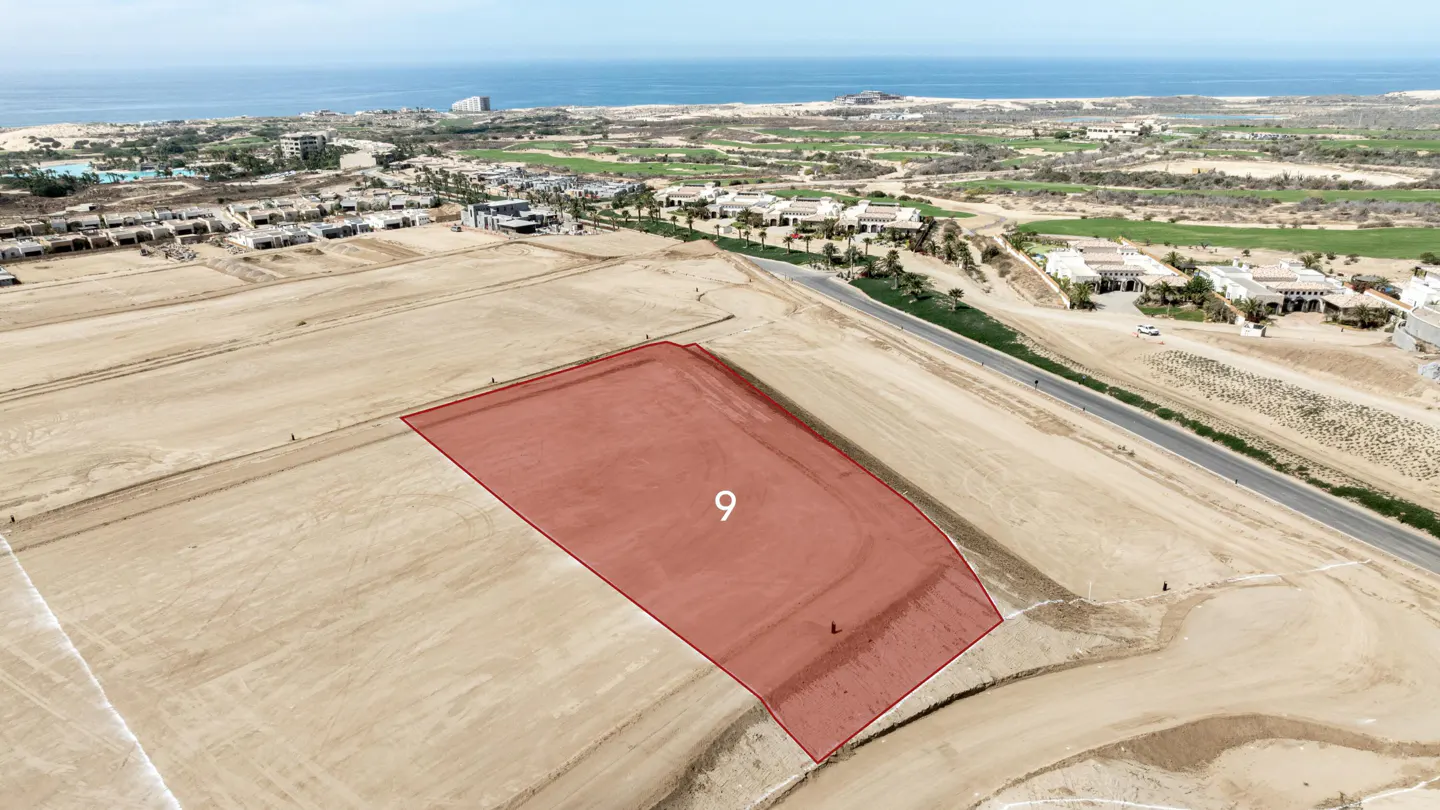 Aerial view of a vacant, sandy building lot highlighted in red and labeled number 9, near a coastal resort and ocean.