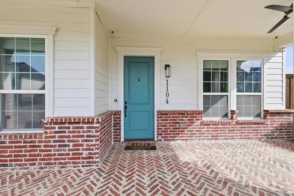 Front porch of a house with a turquoise door, brick floor, and white siding. The house number 1104 is visible.