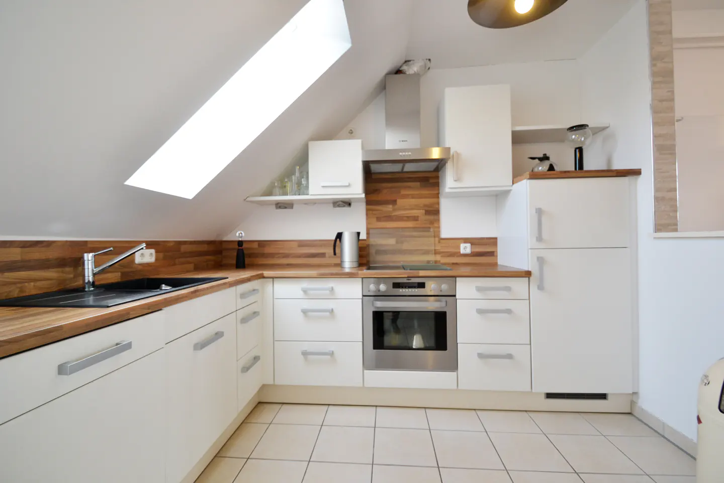 Bright kitchen with white cabinets, wood countertops, and stainless steel appliances under a sloped ceiling with a skylight.